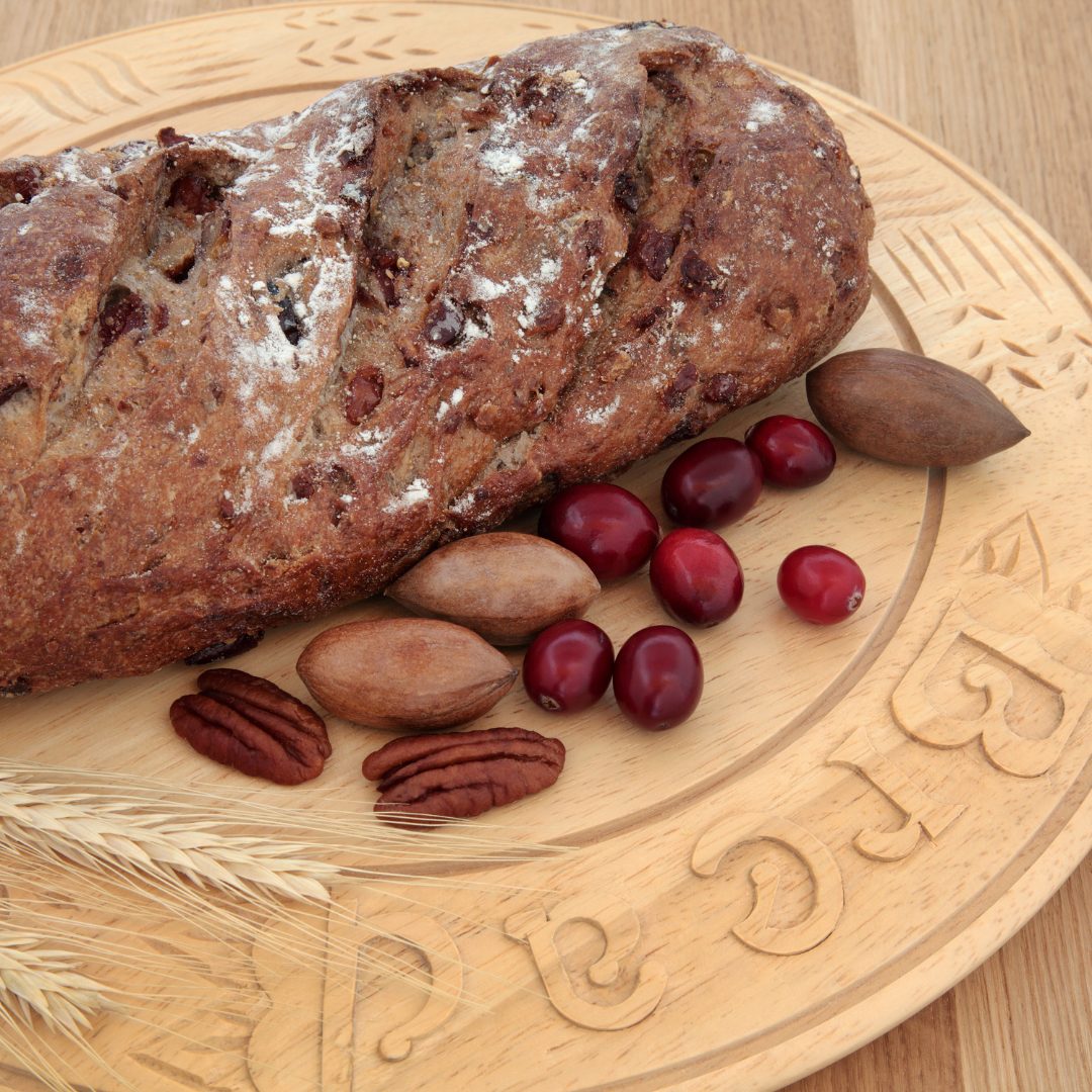 Vegan cranberry pumpkin bread on wood plate. Pecans and cranberries are placed at the forefront.