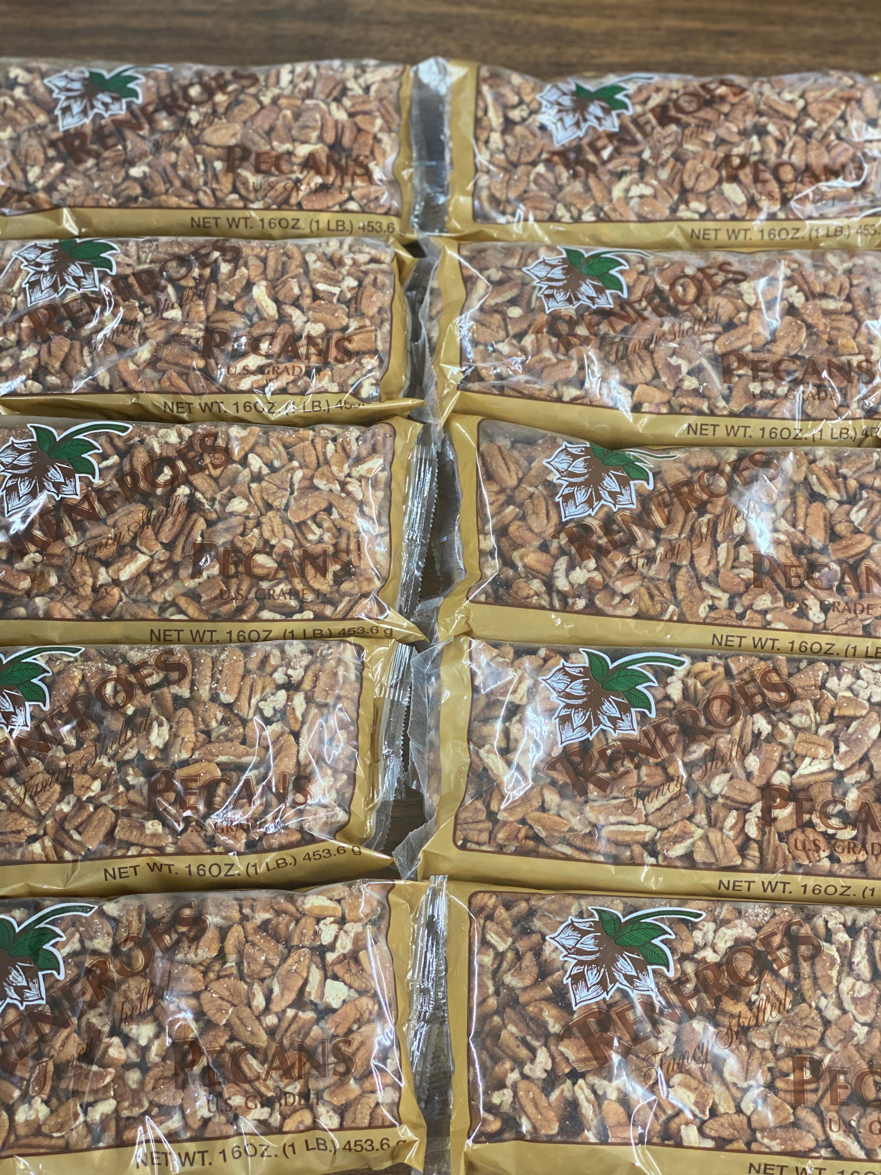 Multiple 1 pound bags of large pecan pieces with Renfroe Pecan Company logo displayed on a wood table